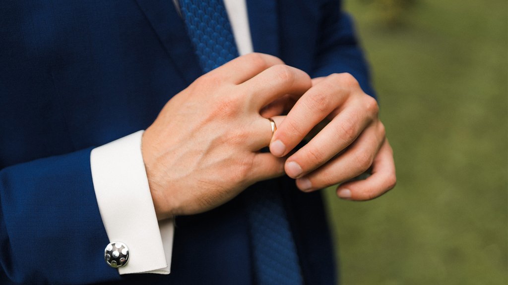 A man in a dark blue suit is wearing a men's ring