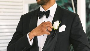 A man's ring is worn on the hand of a man in a black suit.