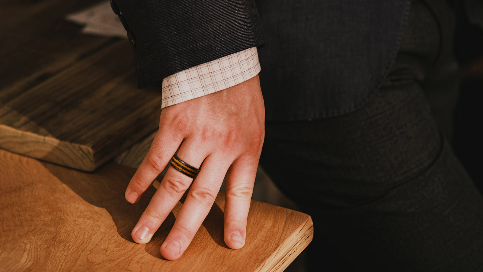 Man in a suit leaning on a wooden table with a wooden ring on his hand