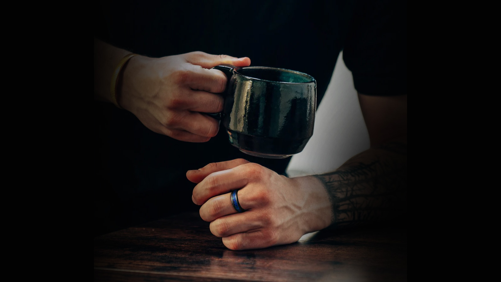 The man holds a cup in one hand and wears a blue meteorite ring in the other