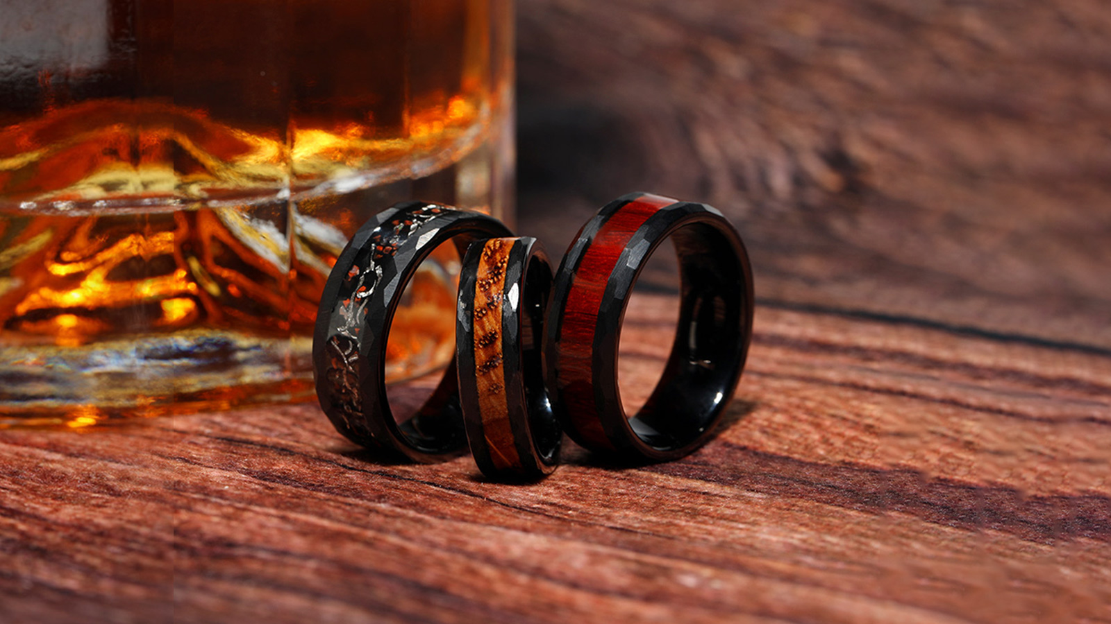 Three black men's wedding rings, with various inlays, were placed on a wooden table