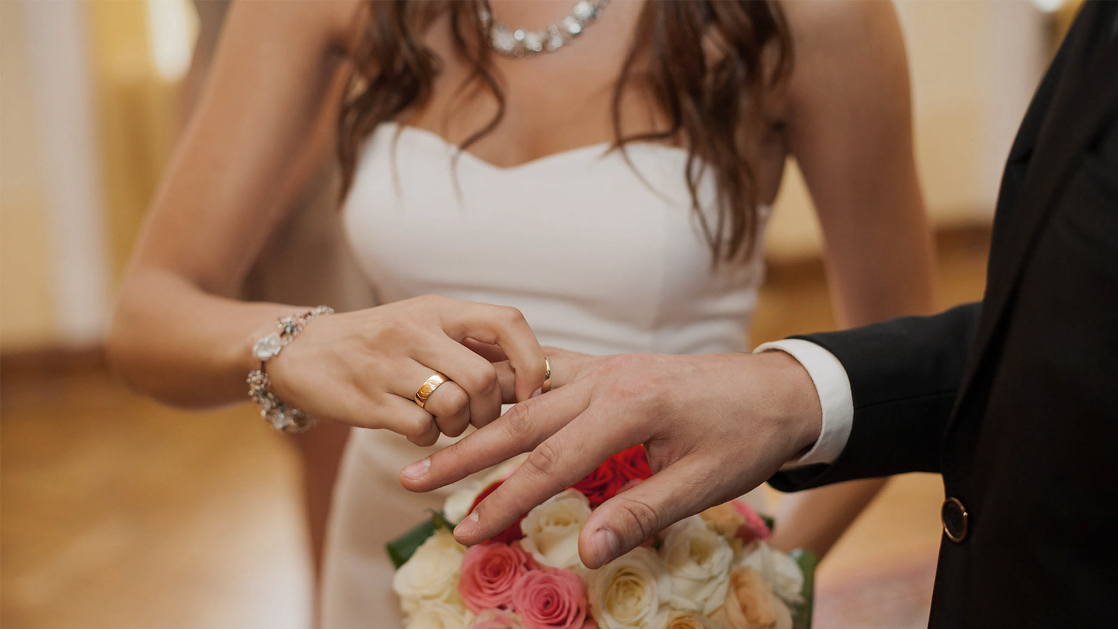 A woman in a wedding dress is putting on a wedding ring for the groom
