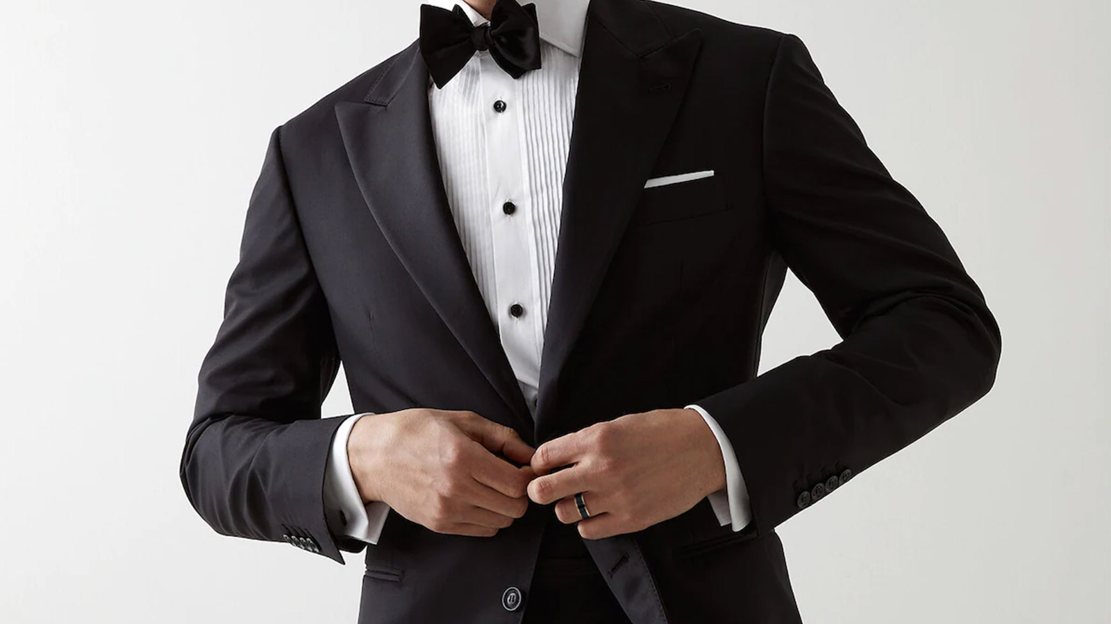 The man in the black suit is unbuttoning his buttons and wearing the man's wedding ring on his hand