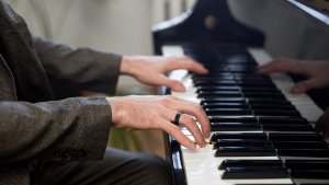 A man with a titanium ring on his finger is playing the piano