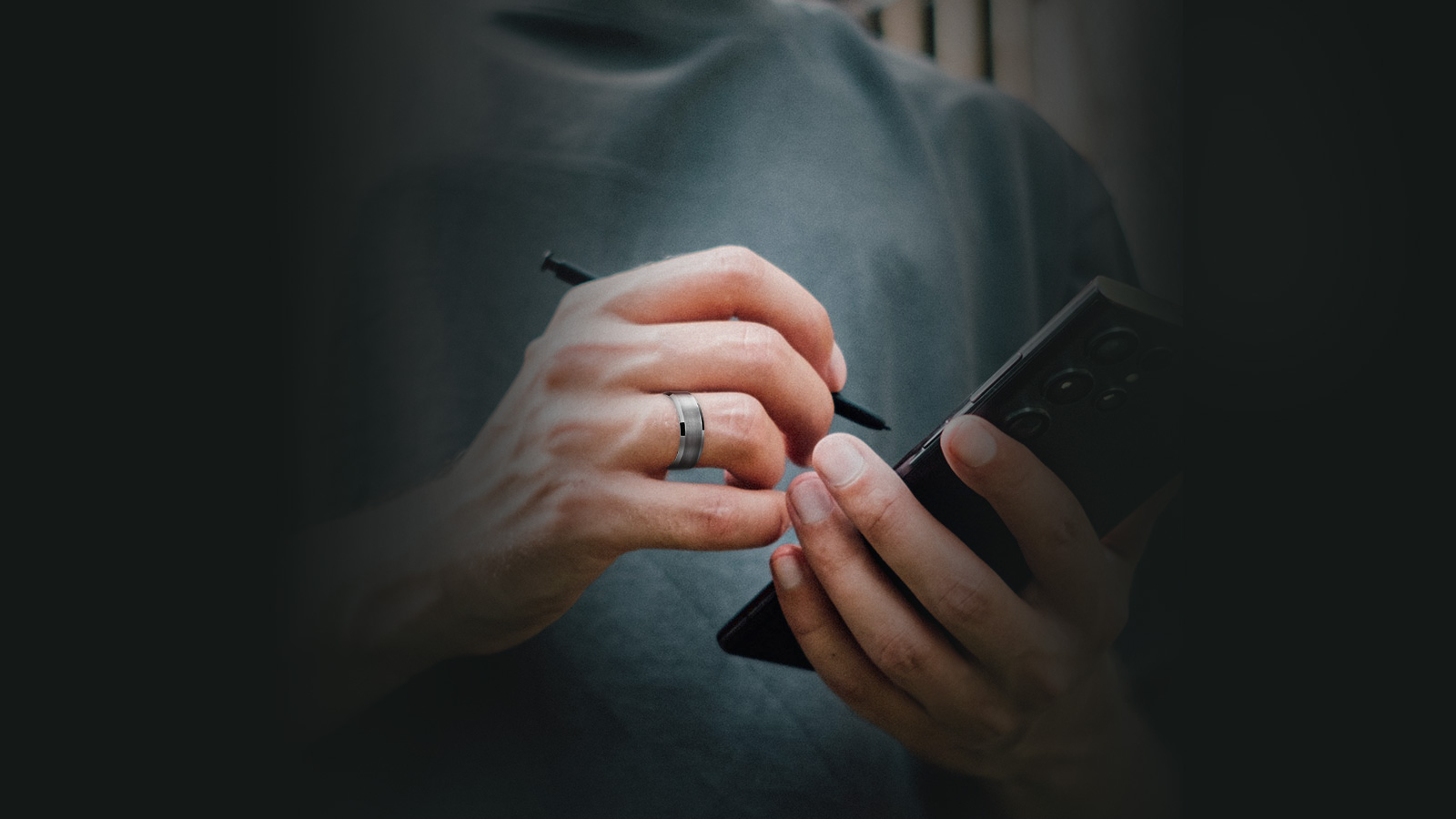 The man in the blue T-shirt is using a stylus on his phone and has a tungsten ring on his hand