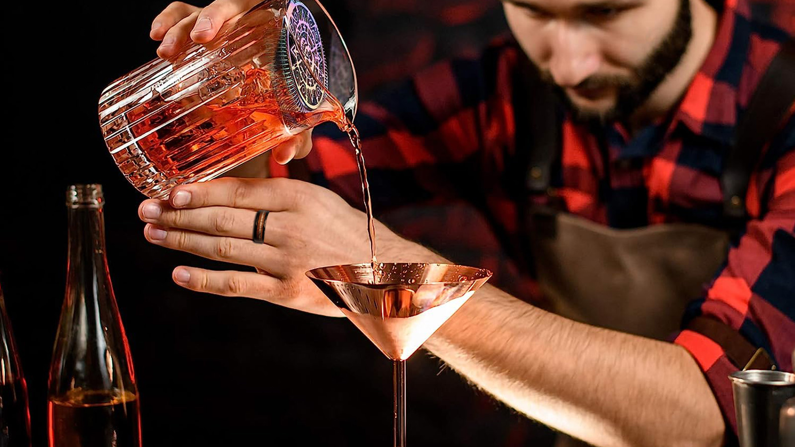 A man in a plaid shirt with thick black rings is mixing a cocktail