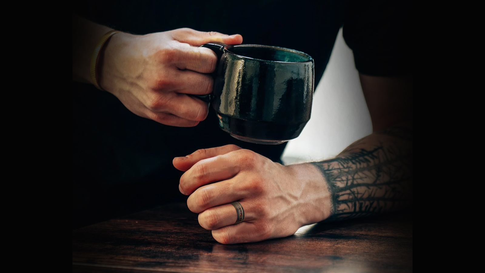 The man holds a water cup in his right hand and a dinosaur bone ring in his left