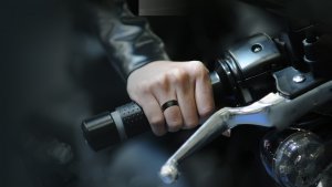 The man's hand holds the handlebar of the motorcycle, and he wears a black men's ring on his finger