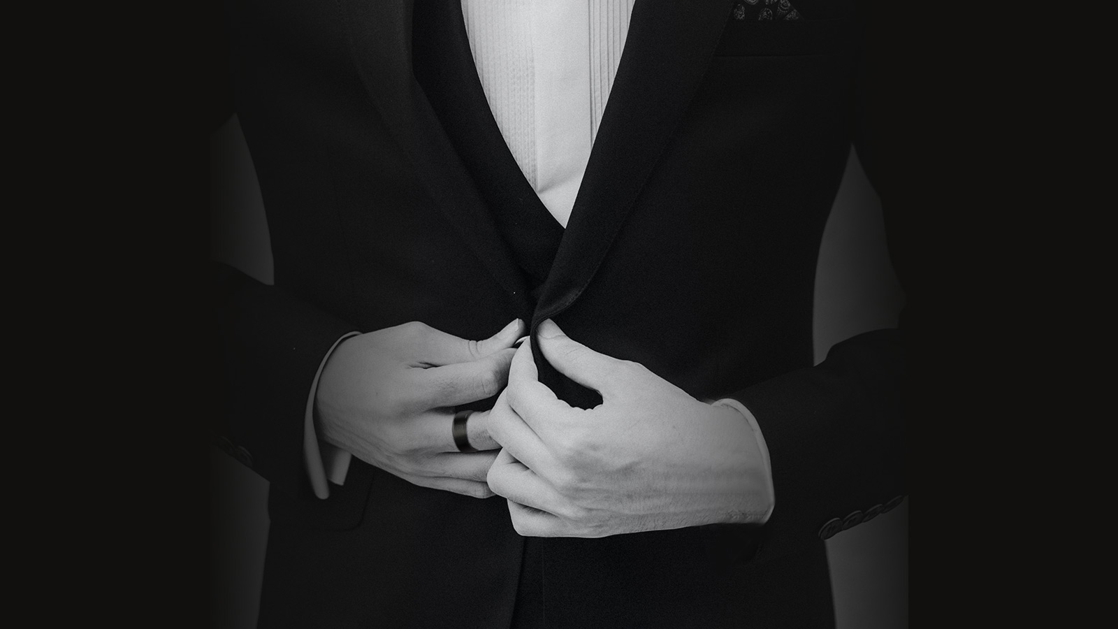 A man in a suit wears a black men's ring on his hand, a close-up picture in black and white tones