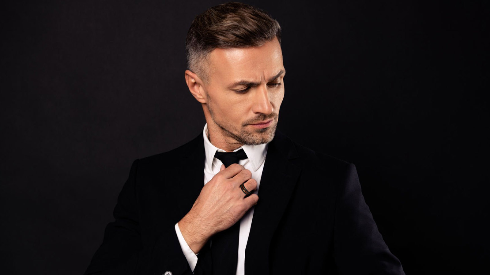 A stylish man in a black suit with a black men's wedding ring on his finger